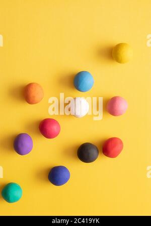 Viele verschiedene farbige Plastilin Kugeln auf gelbem Hintergrund. Bunte Top-Down-Ansicht, handgerollte Kinderspielzeug Stockfoto
