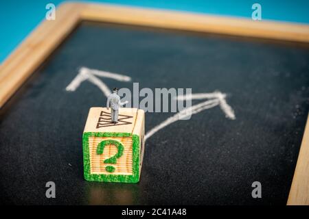 Geschäftskonzept: Entscheidungsfindung. Miniatur-Mann auf Tafel mit zwei Pfeilen in verschiedene Richtungen Stockfoto