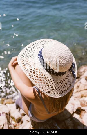 Frau mit Hut sitzt am Strand am Meer Stockfoto