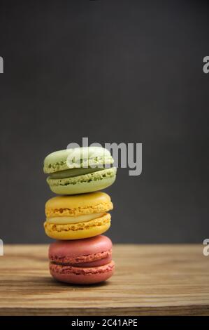 Ein Stapel Makronen in verschiedenen Geschmacksrichtungen und Farben auf einem Holztisch mit dunklem Hintergrund, Seitenlicht und Kopierraum Stockfoto