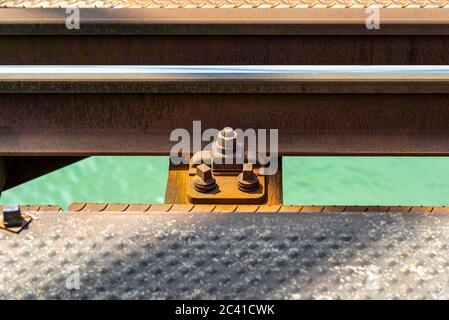 Eisenbahnschienen auf der Eisenbahnbrücke über den Fluss gelegen, Nahaufnahme der Befestigungsschraube, auf Holzschwellen liegend, fließt ein türkisfarbener Fluss und Stockfoto