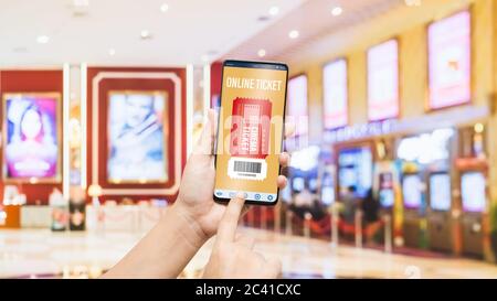 Mockup Handy hand mit Smartphone Kinokarten mit unscharfen Bild der Ticketverkauf zu kaufen Zähler bei Kino mit grafisches Symbol, online Stockfoto