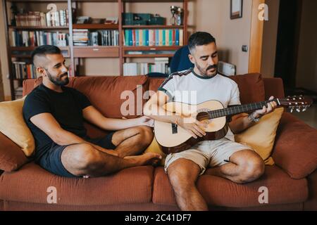 Boy spielt Gitarre auf der Couch sitzt sein Freund Stockfoto