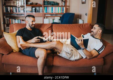 gay paar Lesung auf die Sofa mit ihre Beine auf Einander Stockfoto