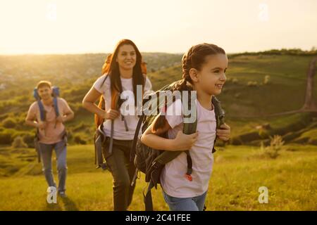 Familie mit Kind und Rucksäcken auf einem Spaziergang in der Natur bei Sonnenuntergang. Stockfoto