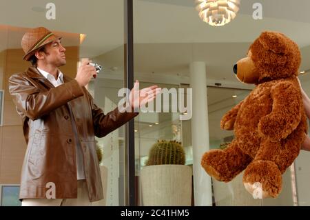 Geschäftsmann in Lederjacke und Hut fotografiert einen großen Teddybären Stockfoto