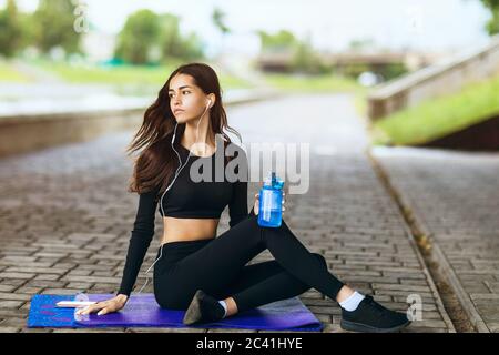 Das Mädchen sitzt auf einem Turnteppich und ruht sich nach dem Sport aus. Gesundes Lifestyle-Konzept. Stockfoto