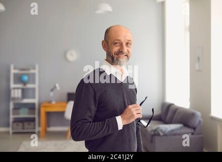 Porträt eines glücklichen älteren Mannes lächelnd, während im Wohnzimmer stehen. Selbstbewusster erfahrener Profi.