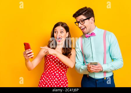 Foto von ziemlich Dame gut aussehend Kerl schockiert direkt Telefon Finger zeigen lustige Bild tragen rot gepunkteten Kleid Hemd Fliege isoliert gelb helle Farbe Stockfoto