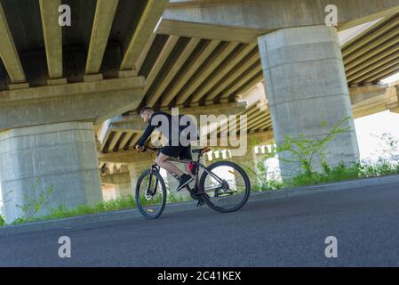 Athlet, bärtiger Radler, fährt auf der Autobahn auf einem Sportfahrrad. Unter der Brücke. Im Freien. Frühjahrssport. Stockfoto