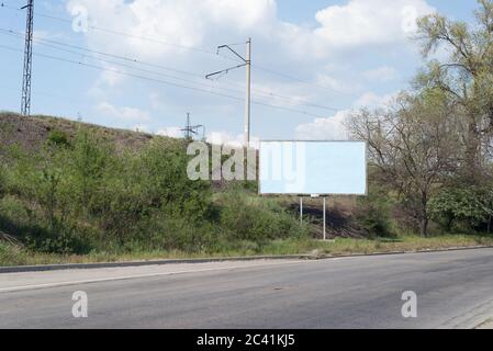 Straßenwerbung, vor dem Hintergrund von grünen Bäumen der Straße, eine leere werbefreie Plakatwand entlang der Straße. Werbung, Schild, leer, Muster Stockfoto