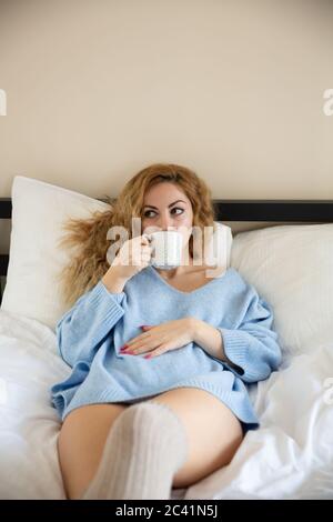 Frau in blauem Pullover mit der Tasse Tee im Bett liegen. Stockfoto