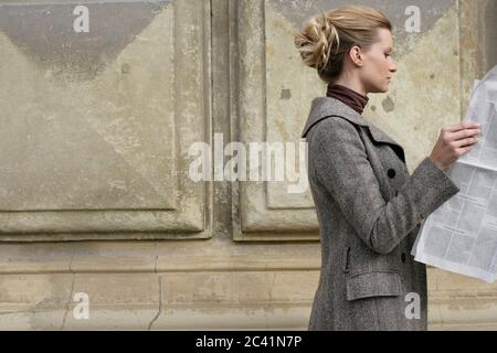 Junge blonde Frau liest Zeitung vor einem Stein Denkmal - antikes Gebäude - Freizeit Stockfoto