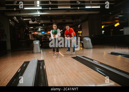 Ein schönes liebend kaukasisches Paar, das Bälle auf der Bowlingbahn wirft. Freund und Freundin im Bowling Club Stockfoto