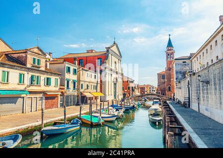 Chioggia Stadtbild mit schmalen Wasserkanal Vena mit bunten Booten, Kirche Chiesa dei Filippini, Turm von Parrocchia di San Giacomo Apostolo Gebäude und Backsteinbrücke, Norditalien Stockfoto