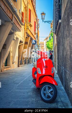 Chioggia, Italien, 16. September 2019: Rotes Motorroller Vespa in enger italienischer Straße im historischen Stadtzentrum, vertikale Ansicht, Region Venetien Stockfoto