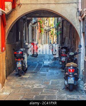 Chioggia, Italien, 16. September 2019: Motorroller Vespa und Motorrad im Bogen der engen italienischen Kopfsteinpflasterstraße im historischen Stadtzentrum, Region Venetien Stockfoto