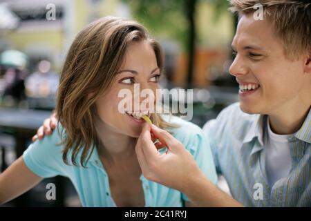 Blonde Mann legt eine französisch braten in den Mund einer jungen Frau - Spaß - Zweisamkeit - Biergarten - Sommer Stockfoto