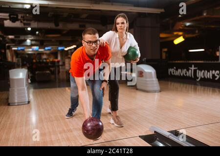 Ein schönes liebend kaukasisches Paar, das Bälle auf der Bowlingbahn wirft. Freund und Freundin im Bowling Club Stockfoto