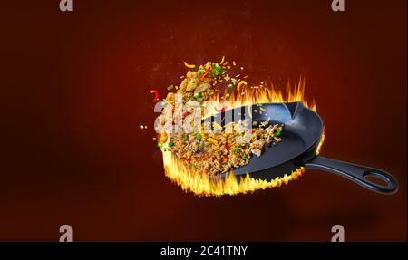 Köstlicher chinesischer gebratener Reis, der in einer heißen, flammenden Pfanne gebraten und in der Luft mit Huhn, Paprika, Erbsen, Karotten und Zwiebeln geschleudert wird. Ansteigender Dampf und Stockfoto