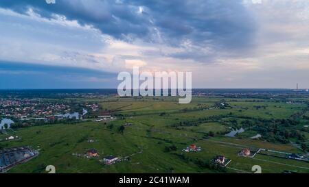 Luftaufnahme von Feldern mit spärlichen Gebäuden in kleinen Privathäusern und mit einer großen Stadt im Hintergrund bei Sonnenuntergang. Stockfoto