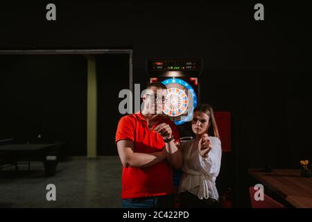 Eine junge schöne kaukasische Frau und ein Mann spielen Darts. Liebe und Erholung Stockfoto