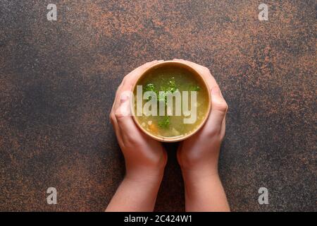 Hühnerbrühe mit Grüns in handgeschenkten Papierbehältern in Kinderhand. Suppe zu gehen, gesunde Ernährung Lieferung. Blick von oben. Stockfoto