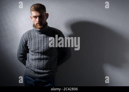 Studio-Porträt eines jungen bärtigen Kerl von fünfundzwanzig Jahren alt. In einem warmen Winterpullover, stolz, grau, schaut weg. Auf schwarzem Hintergrund. In einem Stockfoto