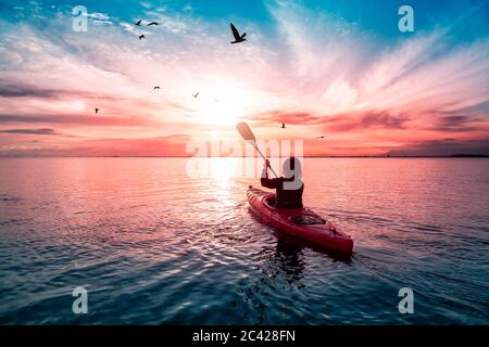 Kajakfahren im ruhigen Wasser bei einem farbenfrohen und lebhaften Sonnenuntergang. Stockfoto