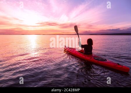 Kajakfahren im ruhigen Wasser bei einem farbenfrohen und lebhaften Sonnenuntergang. Stockfoto