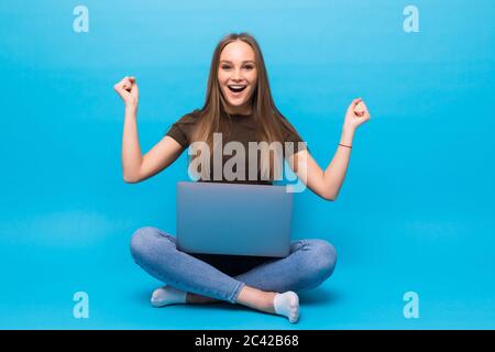 Emotionale junge Frau mit Laptop feiert Sieg auf farbigen Hintergrund Stockfoto