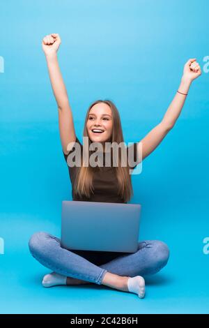 Emotionale junge Frau mit Laptop feiert Sieg auf farbigen Hintergrund Stockfoto