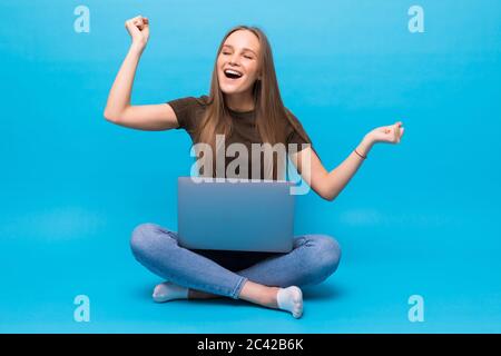 Emotionale junge Frau mit Laptop feiert Sieg auf farbigen Hintergrund Stockfoto