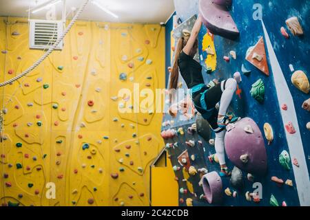 Junge Frau, die eine große, von Männern gemachte Kletterwand klettert Stockfoto