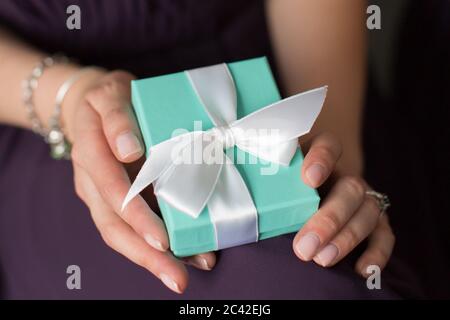 Frau Hände halten ein Geschenk. Geschenkbox mit weißer Schleife Stockfoto