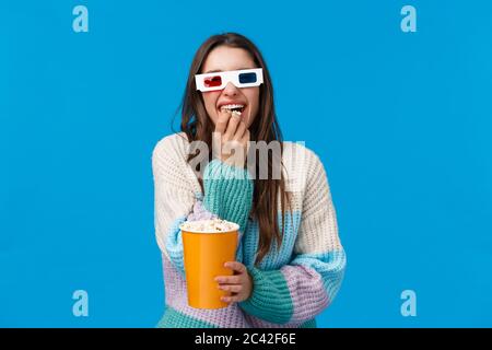 Fröhliches und fröhliches, lachendes kaukasisches Mädchen mit einer dreidimensionierten Brille, kicherndem und knallendem Popcorn, einer Halterbox und stehendem Popcorn Stockfoto