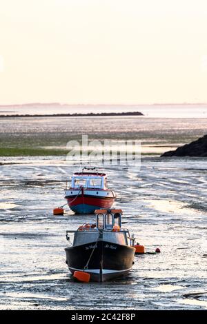 Zwei kleine Fischerboote auf dem Watt im Hafen von Herne Bay an der englischen Kent Coast, bei Ebbe während der goldenen Stunde kurz vor Sonnenuntergang. Hintergrund dunstig Horizont mit der Isle of Sheppey. Stockfoto