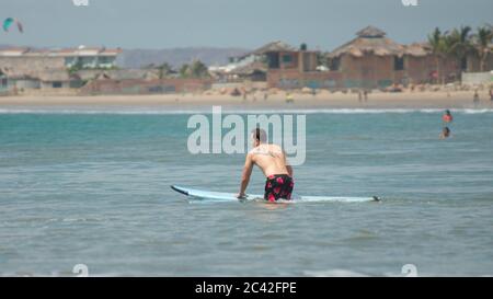 Mancora, Piura / Peru - 9. April 2019: Junger Mann, der an einem bewölkten Tag mit einem Surfbrett vor dem Dorf ins Meer kommt Stockfoto