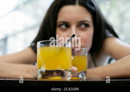 Eine junge Frau sitzt vor zwei Gläsern Limonade und sieht - Freizeit - hinterlickig - Schwimmbad Stockfoto
