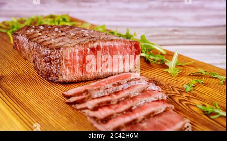 Köstliches und gesundes gegrilltes mittelseltenes Rindersteak auf Holzbrett mit Rucola. Stockfoto