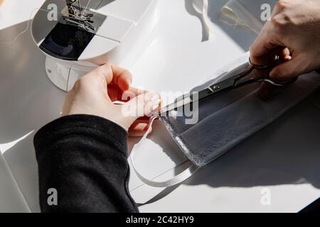 Hoher Winkel der Ernte weiblichen Schneidfaden in einem Stoff Schutz Gesichtsmaske zu Hause Stockfoto