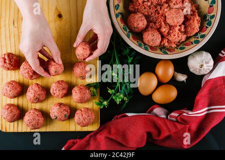 Frau macht hausgemachte Fleischbällchen mit Hackfleisch gewürzt mit verschiedenen Gewürzen für den Geschmack. Stockfoto