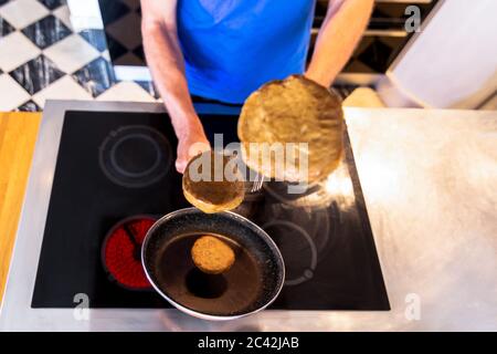 Mann Kochen hält eine Pfanne mit Seitan Burger fliegen in der Luft mit selektivem Fokus. Veganes Konzept Stockfoto