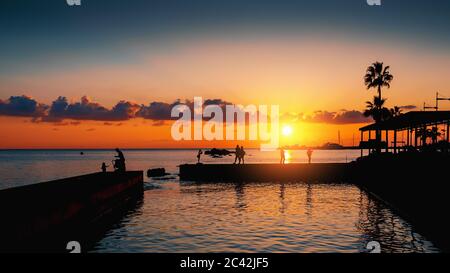 Dramatischer Sonnenuntergang über mittelmeer und Silhouette des Piers mit unkenntlichen Touristen, romantische Stimmung. Stockfoto