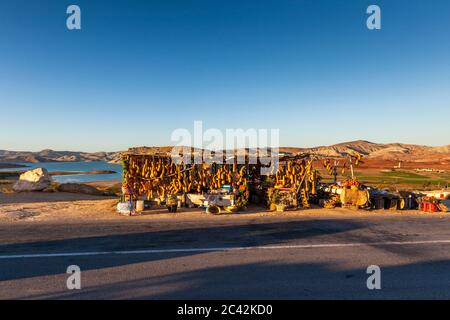 Ein hölzerner Straßenverkaufsstand mit langen getrockneten Produkten steht über dem Stausee Barrage Sidi Chahed in der Nähe von Meknès, Marokko, ein großer Felsbrocken liegt im Vordergrund. Stockfoto