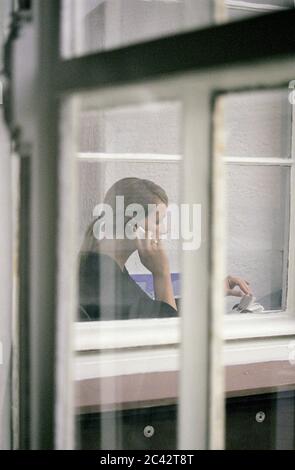 Junge blonde Frau am Telefon (fotografiert durch Fenster) - Büro Stockfoto