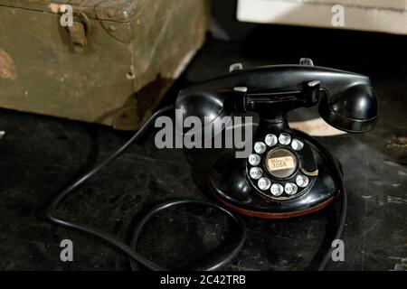 Auf einem Schreibtisch sitzt ein schwarzes Drehtelefon mit aufgeschlungenem Kabel aus den 1940er Jahren. Stockfoto