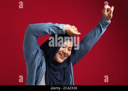 Porträt einer lustigen jungen asiatischen muslimischen Frau trägt roten Hijab tanzen glücklich Ausdruck feiern gute Nachrichten Sieg Erfolg Geste Stockfoto