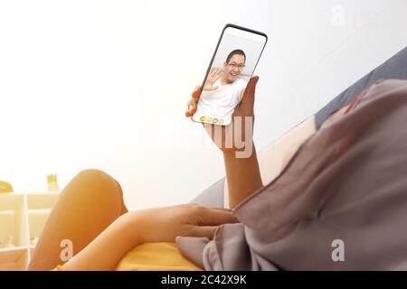 Muslimische Frau, die während ihres Aufenthalts zu Hause wegen einer Coronavirus-Pandemie mit ihrem Mann auf dem Smartphone einen Videoanruf abgab, selektiver Fokus auf das Telefon Stockfoto