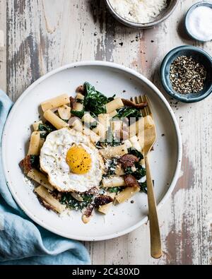 Penne mit Spinat, Speck und einem Spiegelei auf einem Teller. Stockfoto